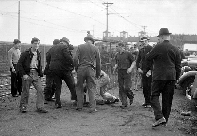 An unidentified UAW organizer is knocked to the ground and beaten by a group of Ford Service Department employees during the Battle of the overpass. Third from left with his back to the camera is Sam Taylor.