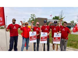 A line of Unifor members with On Strike placards holding their fists in the air