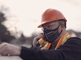 Worker wearing hard hat, safety vest and mask holding field telephone. 