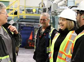 Lana Payne and Gavin McGarrigle in high visibility vests and hard hats sharing a laugh with two members in an industrial setting.