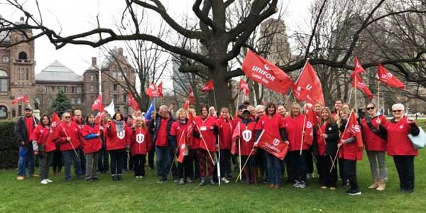 Unifor delegation in front of the legislative building, wearing red Unifor shirts waving our flags.