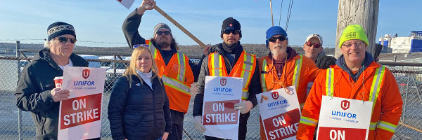 Members of Unifor Local 100 wearing high-visibility vests and holding ‘ON STRIKE’ signs stand together outside of Autoport in Halifax.
