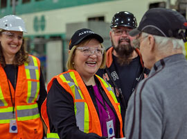 Lana Payne wearing a hard hat and safety goggles smiling and shaking hands with a member with others close by looking on.
