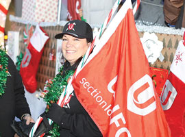 A smiling woman holding a Unifor flag and a large novelty candy cane.